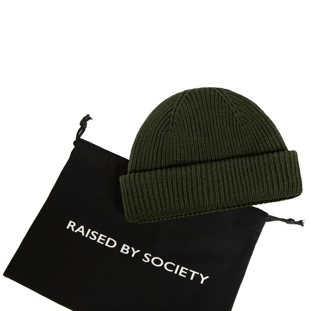 fisherman beanie not too warm. Green beanie on a black drawstring bag with 'Raised by Society' text on a white background. 