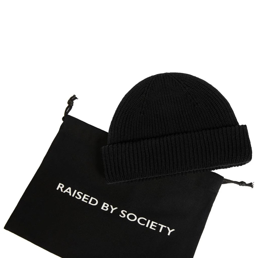 fisherman beanie for mild weather. Black beanie on a black drawstring bag with 'Raised by Society' text on a white background