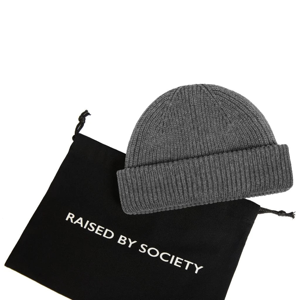 Everyday fisherman beanie cotton. Black dust bag with RAISED BY SOCIETY on it. Dark grey beanie on top. White backgorund.