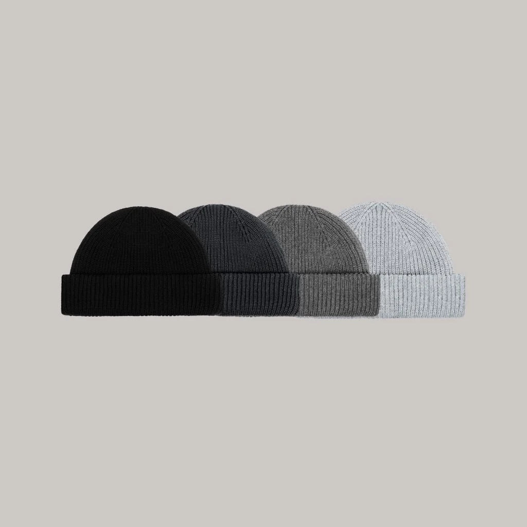 what fisherman beanie is not too warm? The fisherman beanie pro. Made of cotton. Four knit beanie hats in black, gray, and blue on a light gray background